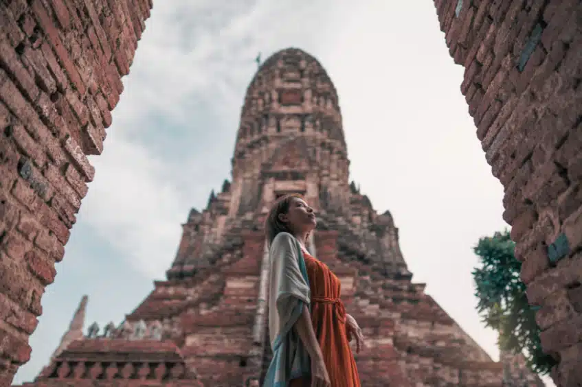Low angle view of the central prang of Wat Chaiwatthanaram in Thailand. A woman stands in the foreground, framed by brick structures.
