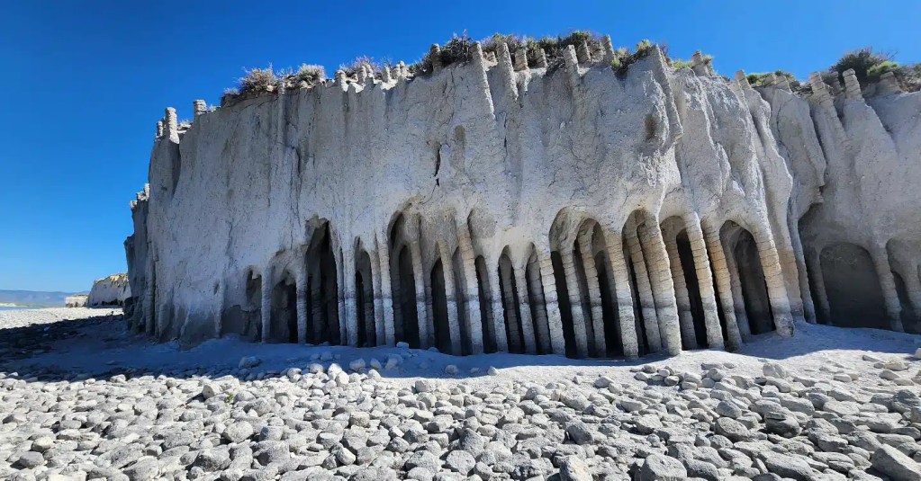 Dramatic natural formations at the Mono Lake Tufa State Natural Reserve in California, featuring tall, white limestone towers and arches surrounded by rocky terrain.