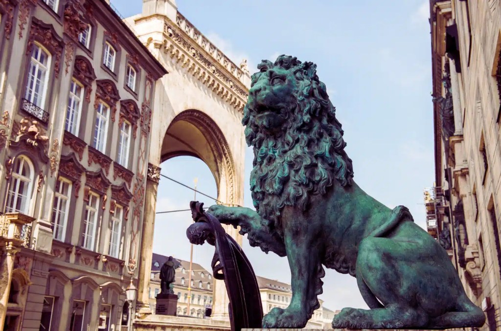 A peaceful scene in Munich featuring the stoic Bavarian Lion sculpture and the city's architecture.