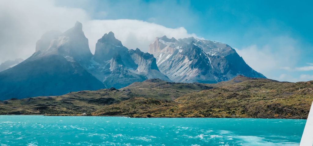 Scenic view of the turquoise waters of Lago Pehoé with the rugged peaks of the Cuernos del Paine in the background, under a partly cloudy sky in Torres del Paine National Park.